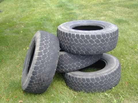 1988 Ford Bronco - Stack of four used tires sitting on the grass.