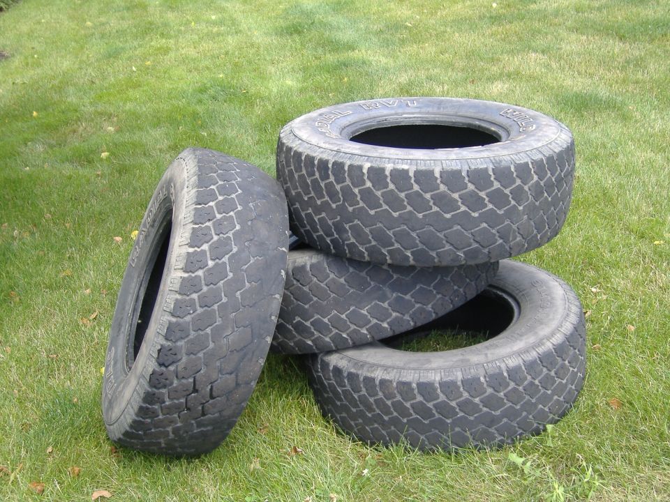 Four used tires stacked on a grassy lawn