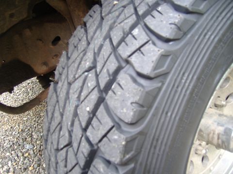 1988 Ford Bronco - Extreme close-up of the tread face on a nearly new all-terrain tire, showing the blocky lug pattern and siping across the full width. A slo…