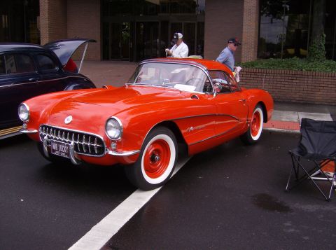 1970 Ford Ranchero - A bright red 1956 Chevrolet Corvette is parked next to a dark-colored sedan at an outdoor event.