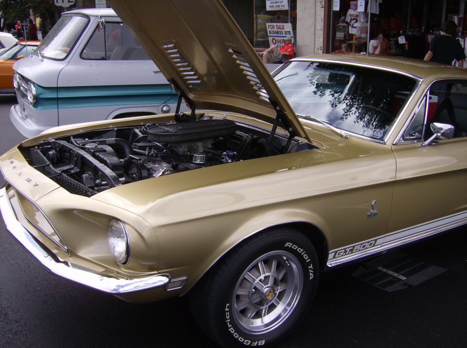 Gold 1967 Shelby GT500 with hood open, showing engine. White stripe on side. "GT 500" visible