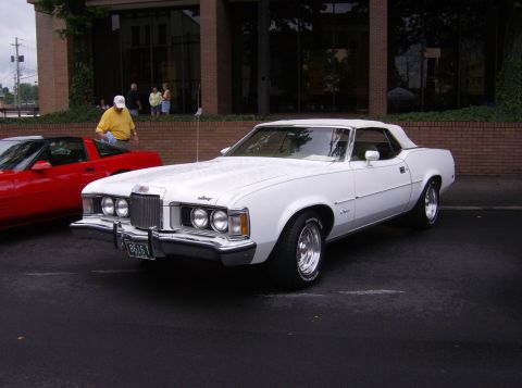 1970 Ford Ranchero - A white convertible parked next to a red sports car in front of a brick building.