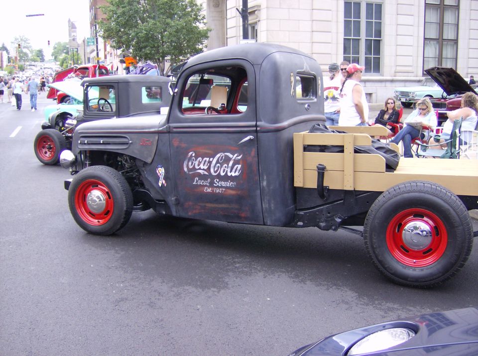 Rat rod truck with Coca-Cola livery and red wheels, seen from the front-three-quarter view