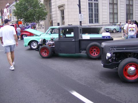 1970 Ford Ranchero - A black hot rod pickup truck with red wheels is parked on a street, with other vehicles nearby.