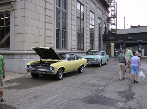 1970 Ford Ranchero - Two vintage cars, a yellow coupe and a light blue station wagon, are parked outside a building.