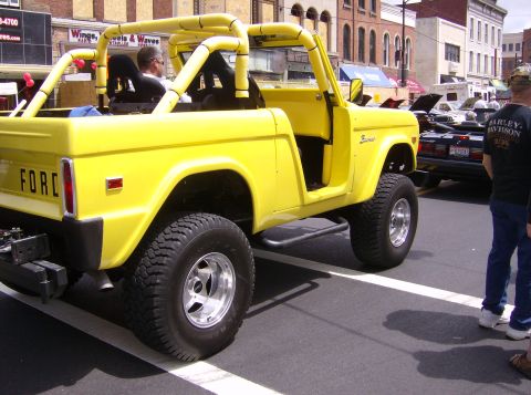 1970 Ford Ranchero - A bright yellow Ford Bronco with a roll cage is parked on a street, with another vehicle visible behind it.