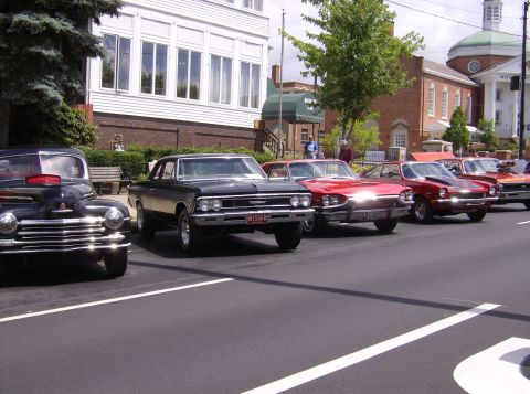 1970 Ford Ranchero - A line of classic cars is parked on a street, with a black coupe in the foreground.