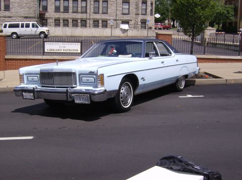 1970 Ford Ranchero - A light blue 1975 Mercury Marquis is parked in front of a brick building, with a white van visible in the background.
