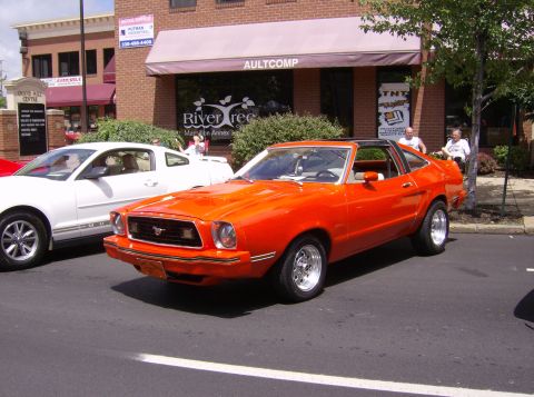 1970 Ford Ranchero - An orange coupe with a black t-top roof is parked next to a white car on a street.