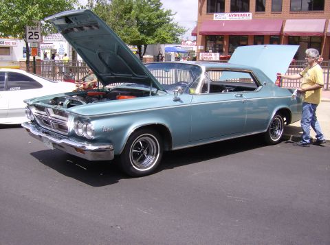 1970 Ford Ranchero - A light blue 1963 Chrysler Newport coupe is displayed with its hood and trunk open at an outdoor car show.