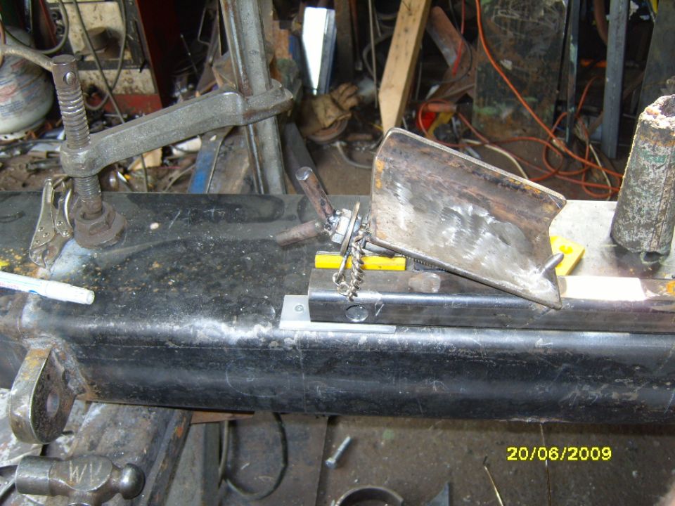 metal piece clamped to a black beam, being worked on with tools