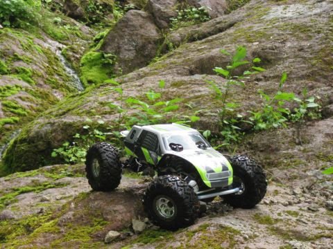2010 Ford Pickup - A remote control rock crawler with green and silver accents navigates a rocky, moss-covered terrain.