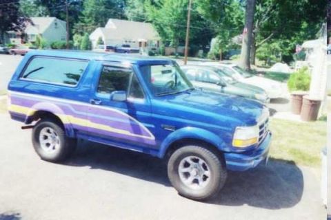 1990 Ford Bronco - This blue SUV features a distinctive purple and yellow stripe graphic along its side.