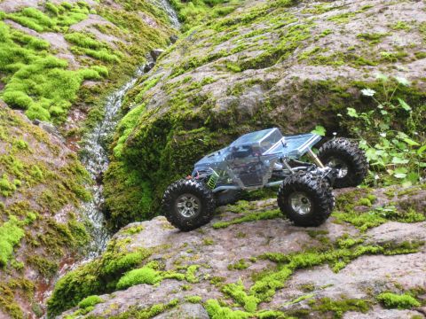 2010 Ford Pickup - An RC rock crawler navigates a rocky, moss-covered terrain with a small stream nearby.