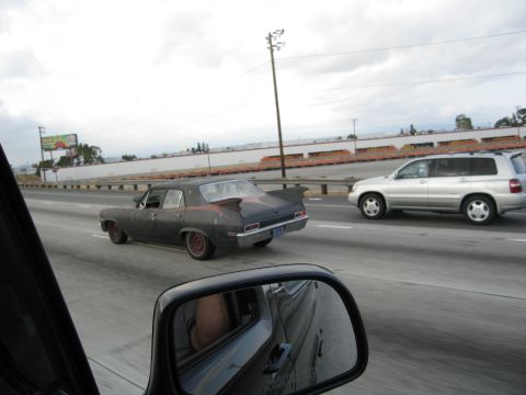 1986 Ford Bronco - A dark sedan with a custom spoiler drives down the highway, seen from the perspective of another vehicle.