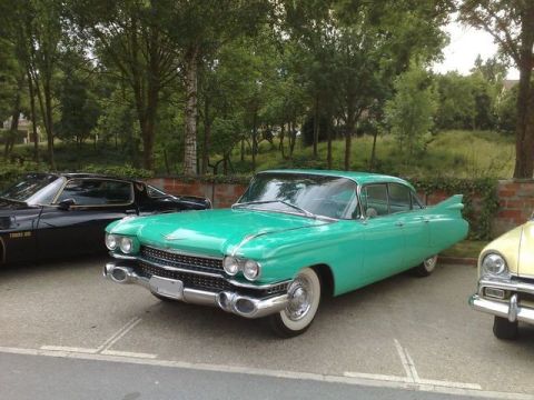 1991 Ford LTD Crown Victoria - A turquoise 1959 Cadillac sedan is parked between a black car and a yellow car, with trees in the background.
