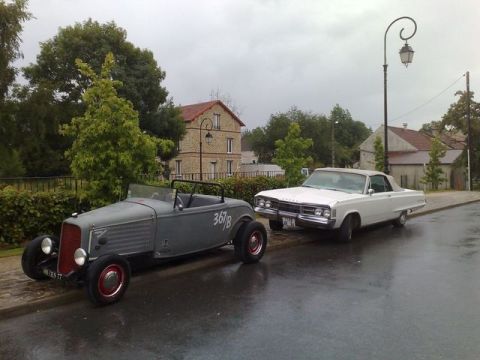 1991 Ford LTD Crown Victoria - A white 1967 Dodge Monaco convertible and a gray hot rod sit parked on a wet street under an overcast sky.