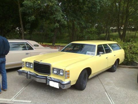 1991 Ford LTD Crown Victoria - A yellow station wagon from the mid-1970s is parked outdoors next to another vehicle.