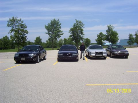 2003 Ford Crown Victoria - A man stands with four police interceptor sedans parked in a lot on a sunny day.
