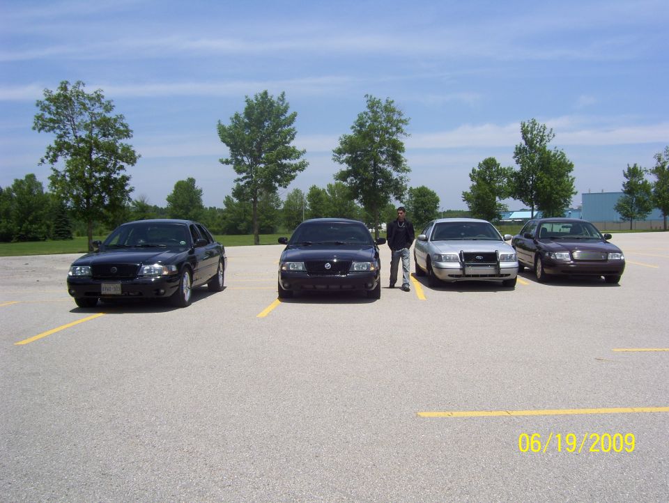 Four police interceptor sedans parked in a lot with a guy standing between two of them