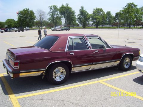 2003 Ford Crown Victoria - A maroon sedan with chrome trim and aftermarket wheels is parked in a lot.