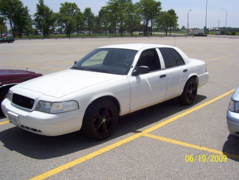 2003 Ford Crown Victoria - A white 2003 Ford Crown Victoria is parked in a lot, with another vehicle visible to the right.