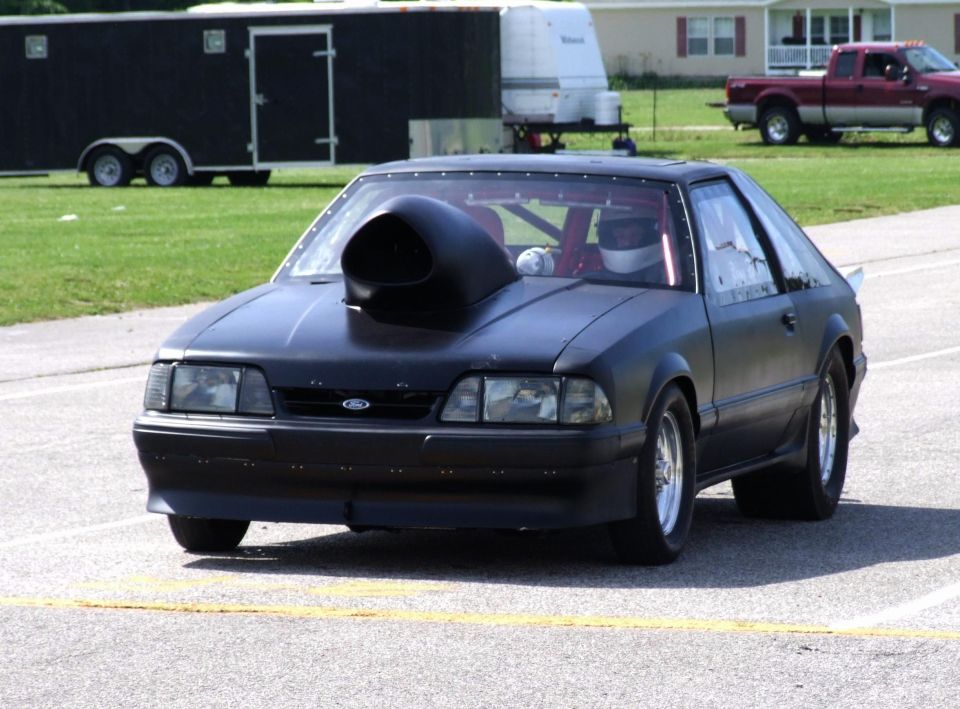 Black drag car with a large hood scoop, driver in helmet, on a track