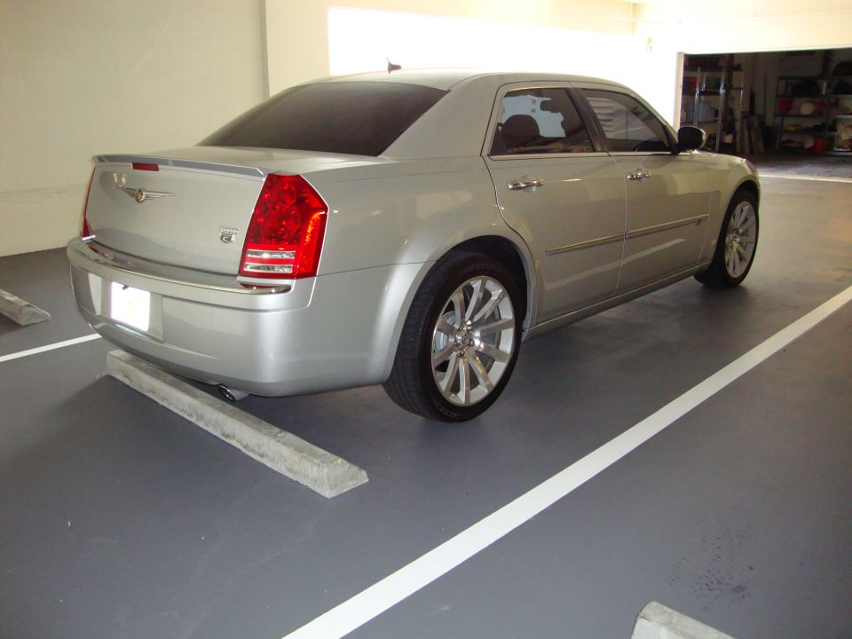 Silver Chrysler sedan parked in a garage, rear view. Chrome wheels and spoiler visible