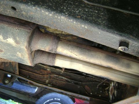 1979 Ford Bronco - Close-up view of the undercarriage, showing dual exhaust pipes and a tire, with visible rust and readable text on the tire.