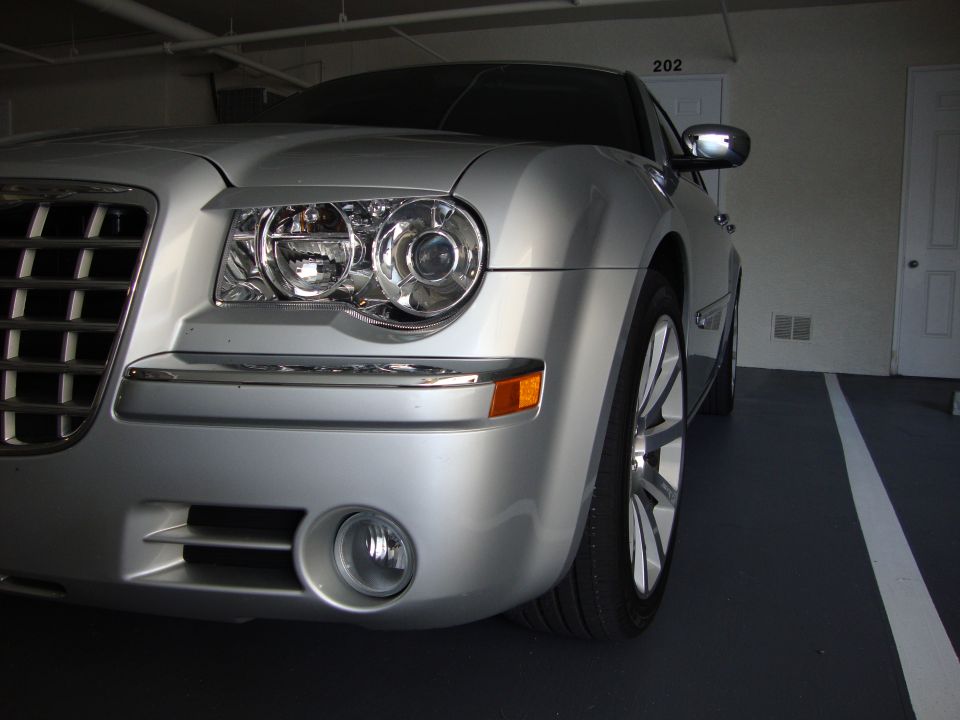 Close front corner of a silver Chrysler 300 showing headlight, chrome grille and fog light