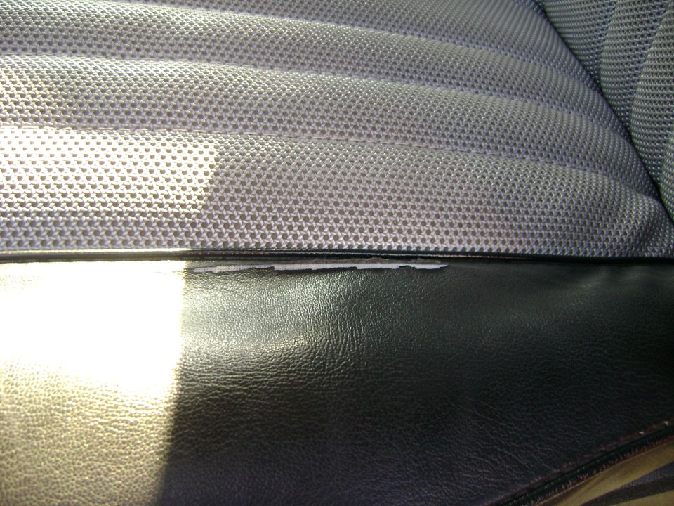 Close-up of a worn car seat with textured gray fabric and black vinyl trim