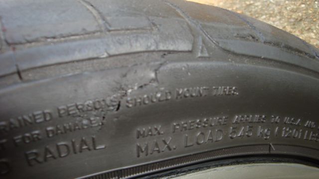 Damaged tire sidewall with visible gouges and cracks