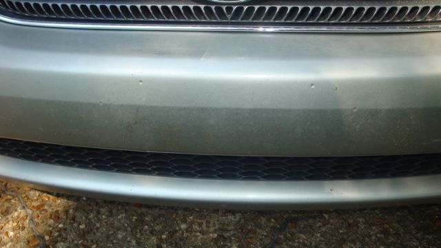Close-up of silver sedan front bumper between chrome grille and black honeycomb lower intake