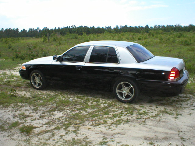 Black four-door sedan in profile with tinted windows and aftermarket wheels parked in a grassy clearing