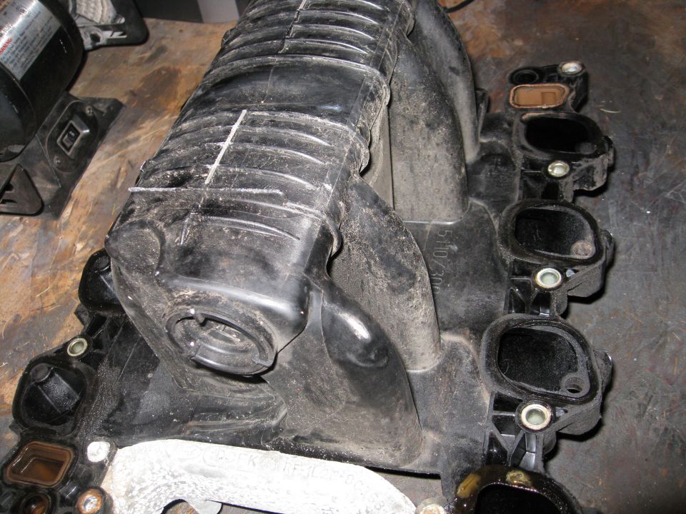 Close-up of a black plastic engine intake manifold with some white markings on it