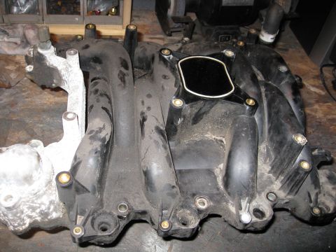 1996 Mercury Grand Marquis - A black plastic intake manifold with a silver metal component is shown, likely a replacement part for a vehicle.