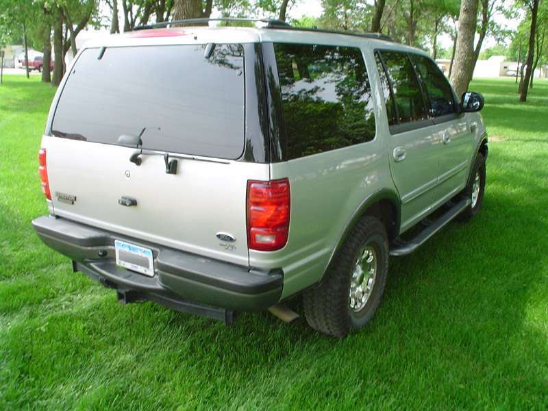 Silver Ford Expedition SUV seen from rear 3/4 angle, parked on grass