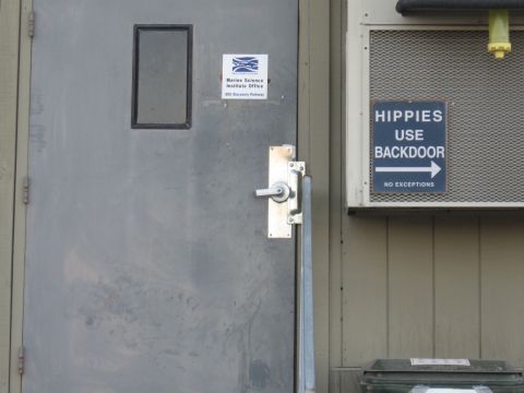 1991 Ford Bronco - Gray metal exterior door of a Marine Science Institute office at 500 Discovery Parkway, next to a humorous blue sign reading "HIPPIES USE B…