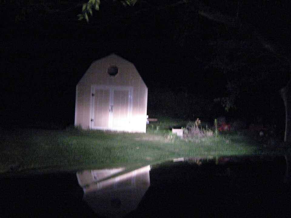 Shed with lights on, reflected in water at night. Supermotors.net logo in corner