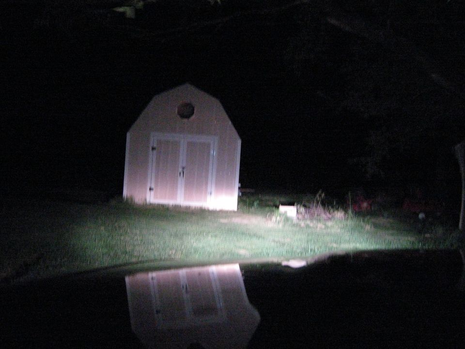 Shed illuminated by headlights at night, reflected in water