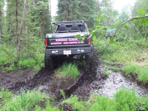 1990 Ford Bronco - A black Ford Bronco navigates a muddy trail in a wooded area.