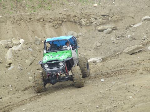 1990 Ford Bronco - A bright green rock buggy with a blue roll cage and roof panel crawls down a rocky dirt pit slope, its long-travel front suspension with re…