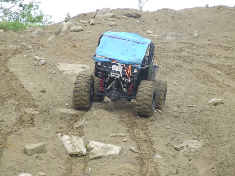 1990 Ford Bronco - Blue tube-chassis rock buggy descending a rocky dirt hillclimb, photographed head-on with its exposed front axle, red coilover shocks, fron…