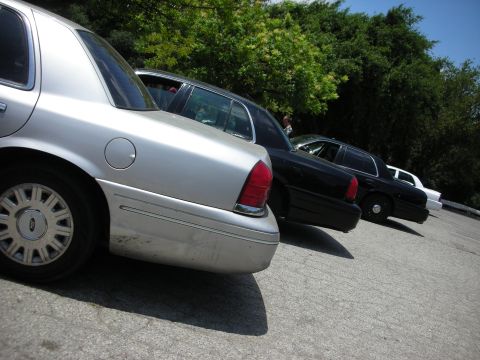 1992 Ford Crown Victoria - Several sedans are parked in a line on a sunny day with trees in the background.