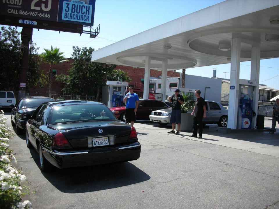 Black sedan with license plate 4TKN250 parked at a gas station with other cars and people