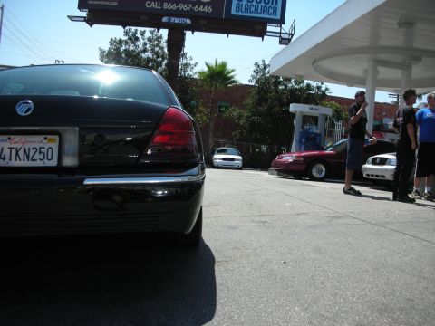 1992 Ford Crown Victoria - A black sedan is parked at a gas station with other vehicles and people nearby.