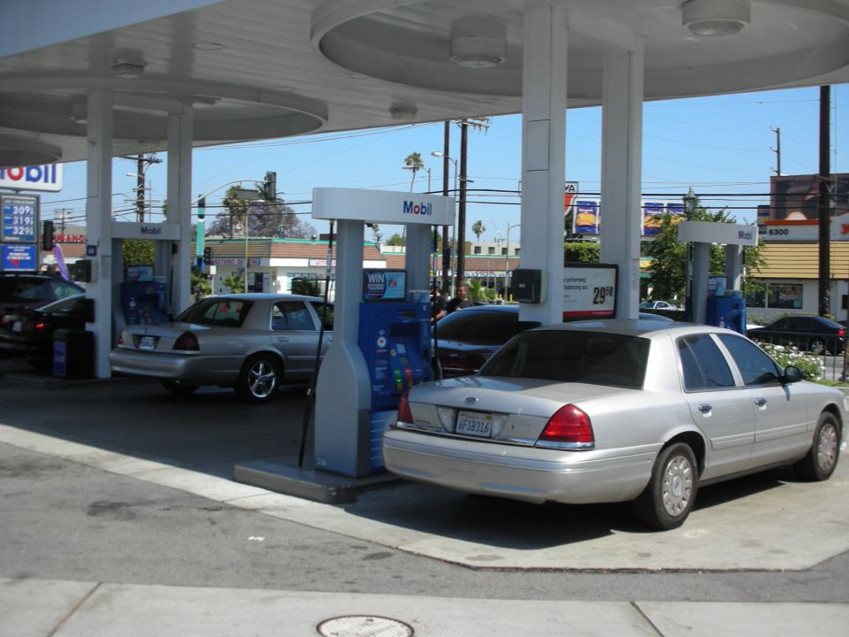 Silver Ford Crown Victoria parked at a Mobil gas station, license plate 6F38316. Another Crown Victoria is visible behind it