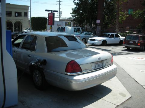 1992 Ford Crown Victoria - A silver sedan is at a gas pump with a fuel nozzle inserted into the tank.