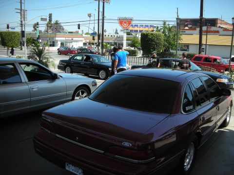 1992 Ford Crown Victoria - A maroon 1992 Ford Crown Victoria sedan is parked next to other vehicles on a sunny day.