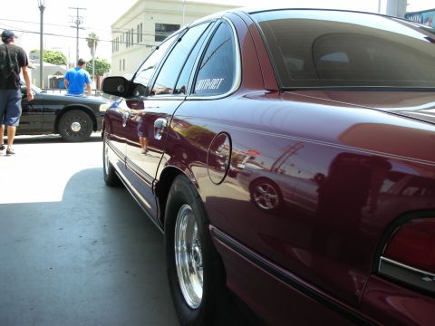 1992 Ford Crown Victoria - A maroon 1992 Ford Crown Victoria is seen from the rear quarter panel, chrome wheels and a sticker on the rear window.